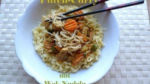 Ein gefüllter Teller mit Putencurry und Wok-Nudeln wird mit Essstäbchen serviert, auf einem hellen Untergrund.