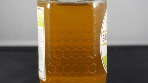 Ein Glas Honig steht auf einem Tisch und reflektiert das Licht, was seine goldene Farbe hervorhebt.