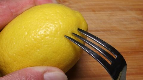 Stich die Zitrone vorsichtig mit einer Gabel an, um ein paar Tropfen Saft zu gewinnen, ohne die Frucht zu zerschneiden. So bleibt die Zitrone länger frisch und du hast jederzeit frischen Saft zur Hand. Eine Gabel sticht in eine Zitrone auf einem Holzbrett, um Zitronensaft freizusetzen.