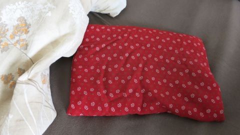 Wenn du Kirschkissen in der Mikrowelle ein bisschen erwärmst, kannst du sie danach unter die Decke legen und die Wärme genießen. Ein rotes Kissen liegt ordentlich auf einem Bett, umgeben von einer weißen Decke, die für ein warmes Bett sorgt.