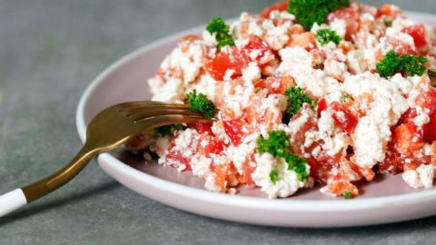 Ein frischer Sommersalat mit Hüttenkäse und Tomaten wird auf einem Teller präsentiert, garniert mit frischem Schnittlauch.