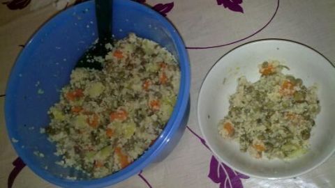 Ein blauer Behälter mit Linsen-Couscous steht auf einem Tisch, während eine Portion auf einem weißen Teller serviert wird.