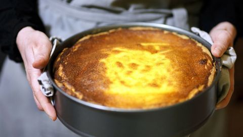 Eine Person hält einen frisch gebackenen, goldbraun gefärbten schwäbischen Käsekuchen in einer Springform.