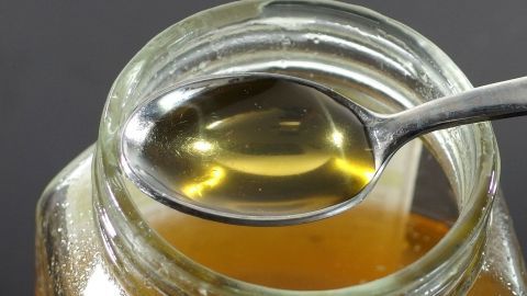 Ein Löffel mit flüssigem Honig steht in einem Glas, während der Honig in der Schale sichtbar bleibt.