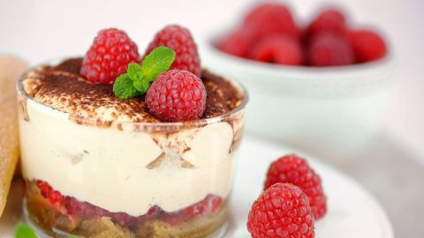 Ein köstliches Zwieback-Beeren-Tiramisu in einem Glas, garniert mit Himbeeren und Minze, auf einem weißen Teller serviert.