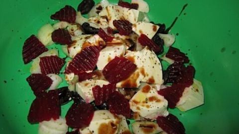 Mozzarella-Würfel liegen bunt gemischt auf einem grünen Teller, umgeben von roter Beete, verfeinert mit Balsamico.