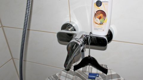 Haarshampoo auf den Fleck geben, etwas verreiben und wie gewohnt waschen. Ein kariertes Hemd hängt an einem Handtuchhalter in der Dusche, während eine Flasche Haarshampoo darüber platziert ist.