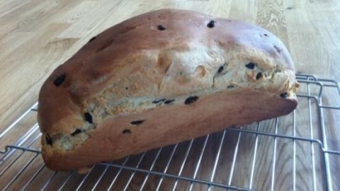 Rosinenbrot kühlt auf einem Gitter auf einem Holztisch ab, mit goldbrauner Kruste und sichtbaren Rosinen im Teig.