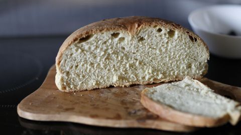 Ein frisch gebackenes Brot liegt auf einem Holzbrett, mit einem Schnitt showing die lockere Krume, ideal für „Brot ohne zu kneten“.