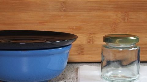 Eine blaue Schüssel und ein leeres Einmachglas stehen auf einer Tischoberfläche, um plastikfreie Alternativen zu zeigen.