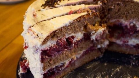 Eine mit Schokolade und Kirschen gefüllte Schwarzwälder Kirschtorte steht auf einem Tisch, einige Stücke sind herausgeschnitten.