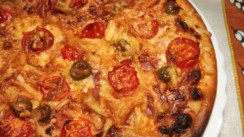 Eine frisch gebackene Pizza mit Tomaten und grünen Oliven liegt auf einem Teller, bereit zum gemeinsamen Essen beim Kindergeburtstag.