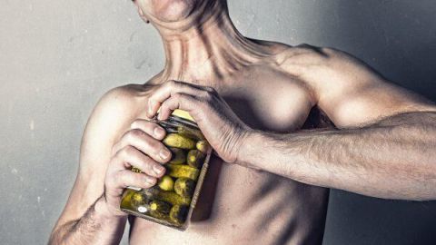 Konservenglas mit Drehverschluss lässt sich leicht öffnen Ein muskulöser Mann versucht, ein Konservenglas mit Drehverschluss zu öffnen, während er angestrengt aussieht.