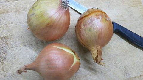 Zwiebeln schneiden: Das "Weinen" gehört mit diesem Tipp der Vergangenheit an! Zwiebeln liegen auf einem Holzbrett, während ein Messer bereitliegt, um sie zum Zerkleinern zu verwenden.