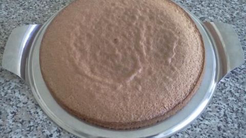 Ein runder Erdbeberkuchen liegt auf einem silbernen Teller und ist bereit für die Vanillecreme-Dekoration auf der Küchentheke.