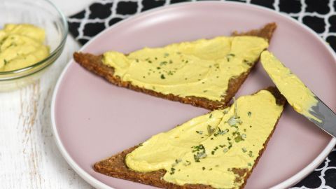 Zwei eckige Brote sind mit einem cremigen Schafskäse-Avocado-Aufstrich bestrichen und auf einem rosa Teller angerichtet.