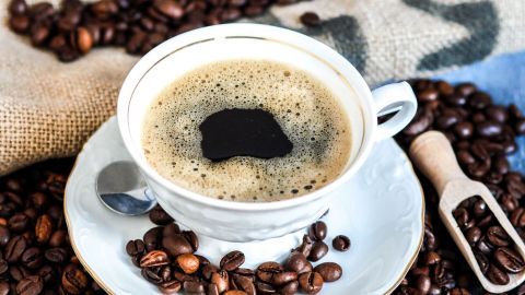 Eine Tasse frischer Filter-Kaffee steht auf einem Unterteller, umgeben von Kaffeebohnen auf einem rustikalen Tuch.