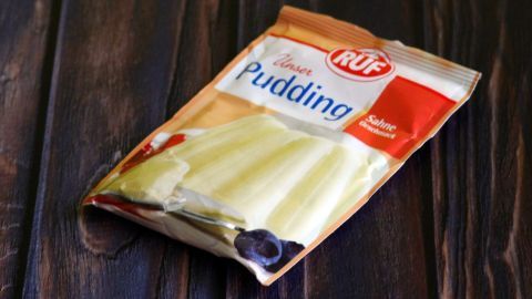 Ein Päckchen Vanillepuddingpulver liegt auf einer dunklen Holzoberfläche und könnte kreativ als Trockenshampoo verwendet werden.