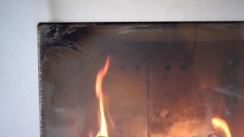 Ein Sichtfenster eines Kamins zeigt flammendes Feuer, während Rußablagerungen im Hintergrund sichtbar sind.
