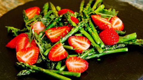 Frischer Spargel und saftige Erdbeeren liegen bunt auf einem schwarzen Teller und bilden einen ansprechenden Salat.