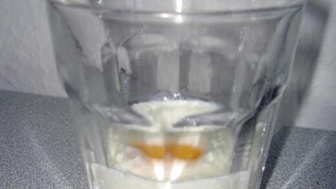 Ein Glas enthält ein rohes Ei, das in Wasser schwimmt, auf einer grauen Oberfläche, bereit für die Zubereitung.