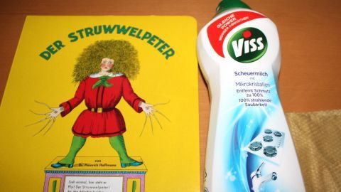 Ein Bilderbuch mit dem Titel "Der Struwwelpeter" liegt nebeneinander mit einer Flasche Viss zum Saubermachen.