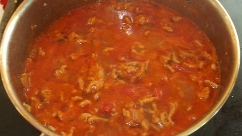 Eine dampfende Tomatensoße "Bolognese" köchelt in einem silbernen Topf auf dem Herd, umgeben von einer einladenden Küchenszene.