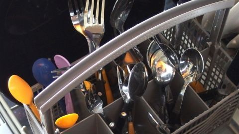 In einem Besteckkorb einer Spülmaschine sind Löffel, Gabeln und Messer ordentlich einsortiert, bereit für den Spülvorgang.
