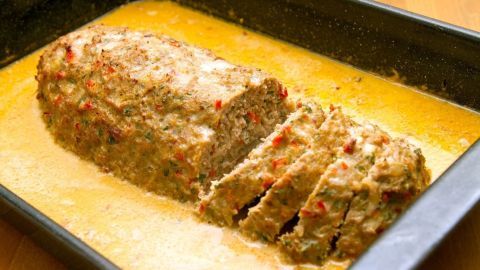 Saftiger Hackbraten liegt in einer Auflaufform, geschnitten und umgeben von einer goldenen Sauce, bereit zum Servieren.