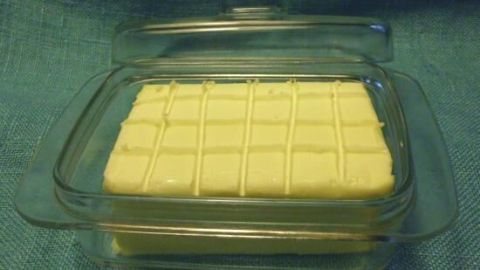 Ein rechteckiges Stück Butter liegt in einer klaren Auflaufform, in gleichmäßige 10-Gramm-Stücke eingeteilt.