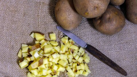 Damit die Steckzwiebeln schön in der Erde bleiben und nicht von Würmern oder sonstigen Tieren herausgezogen werden, kann man kleine rohe Kartoffelstückchen zwischen die Steckzwiebeln streuen. Klein geschnittene, rohe Kartoffelstückchen liegen mit einem Messer auf einem groben Jutesack, umgeben von ganzen Kartoffeln.