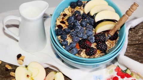 Eine Schüssel Apfel-Rohkost-Müsli mit kernigen Haferflocken, Äpfeln, Beeren und einem kleinen Krug Milch auf einem Tisch.