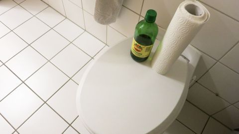 Mit Essigessenz und Küchenrolle Urinstein im WC entfernen: Die einfache, effektive Methode, die dein Badezimmer blitzsauber hält. Der Artikel erklärt, wie du den hartnäckigen Belag ohne aggressive Chemie loswirst. Flasche mit Haushaltsessig und Küchenrolle stehen auf einem WC-Deckel in einem gefliesten Badezimmer.
