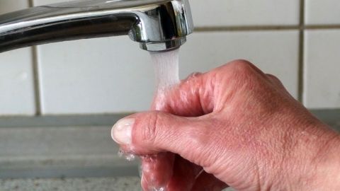 Knoblauchgeruch an den Fingern: Die Finger einfach unter fließendes Wasser halten, und der Geruch ist verschwunden. Eine Hand hält sich unter fließendem Wasser, um den Knoblauchgeruch an den Fingern zu entfernen, in einer modernen Küche.