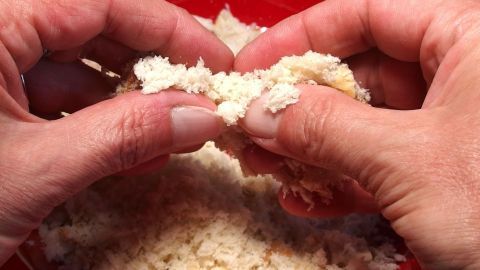 Hände zerreißen frisches Weißbrot über einer Schüssel, um Paniermehl für die Zubereitung von Gerichten herzustellen.