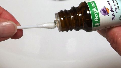 Ein Hand hält einen Wattestäbchen, der in eine Flasche mit Medikament zur Behandlung von Aphten im Mund eintaucht.