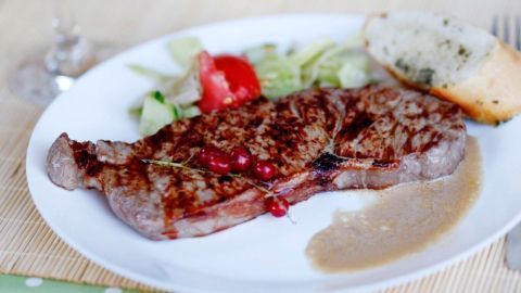 Ein saftiges Steak liegt auf einem weißen Teller, umgeben von frischem Salat und einer Brotscheibe mit Kräutern.
