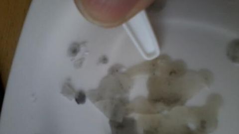 Ein Plastikspatel entfernt Wachs von einer harten, weißen Oberfläche. Der Hintergrund ist leicht unscharf. Keine Text.