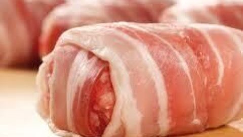 Ein Frikadellen-Röllchen, umhüllt von speckigem Fleisch, liegt auf einem Holzbrett und wartet auf die Zubereitung.