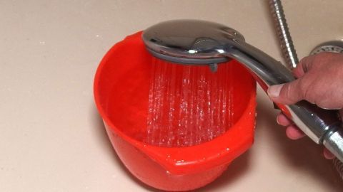 Restwasser sammeln und zum Gießen weiterverwenden - das spart nicht nur Abwassergebühr. Ein orangefarbener Eimer wird mit Wasser gefüllt, während eine Duschbrause darüber gehalten wird, um ihn zum Gießen zu nutzen.