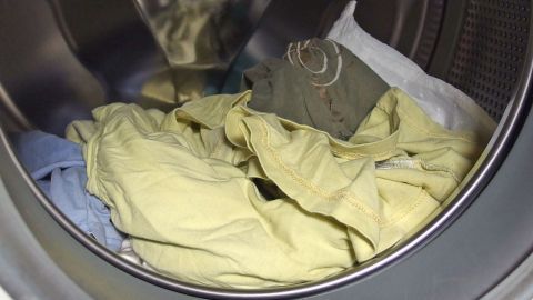 Eine Waschmaschine zeigt gewaschene, zusammengeknüllte Wäsche, die nach dem Waschen aus einer Trommel kommt und möglicherweise stinkt.