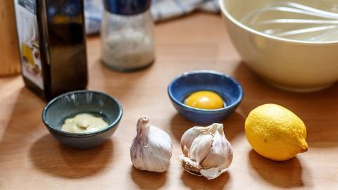 Eine Schüssel und Zutaten wie Knoblauch, Ei, Zitrone und Öl liegen bereit, um Aioli (spanische Knoblauch-Mayonnaise) zuzubereiten.