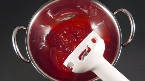 In einem silbernen Topf wird rote Marmelade ohne Stückchen mit einem weißen Pürierstab vermischt, um sie glatt zu machen.