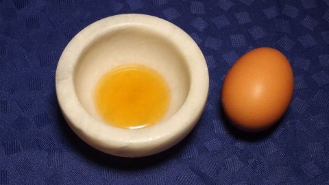 Ein kleiner Mörser mit einem Eigelb daneben, ideal für eine Haarkur gegen trockene, schuppende Kopfhaut.