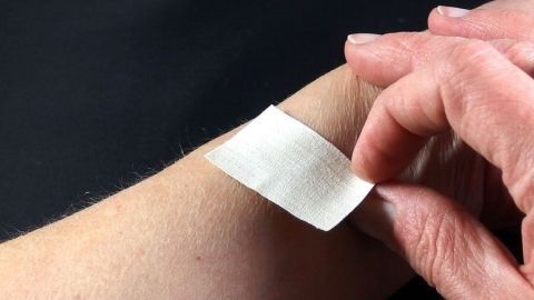 Eine Person zieht ein Pflaster schmerzlos von ihrem Arm ab, während der Hintergrund dunkel ist.