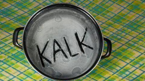 Ein Topf aus Metall zeigt deutlich das Wort "KALK" im Inneren, platziert auf einem karierten Tisch.
