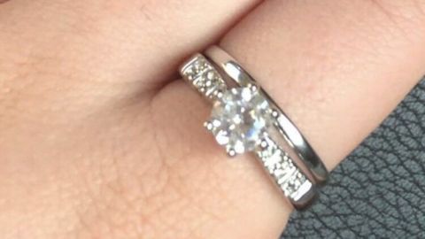 Ein glänzender Ring mit Fimo sitzt auf einem Finger, umgeben von einer strukturierten Unterlage, der Hand ist ruhig.