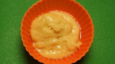 Eine orangefarbene Silikon-Schüssel enthält eine cremige Füllung für Muffins auf einem grünen Tisch.