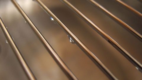 Ein glänzender Grillrost mit Wasserspuren liegt auf einer Oberfläche und weist auf die Reinigung mit Waschsoda hin.