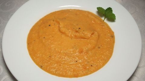 Eine cremige Suppe in einem weißen Teller, frisch püriert, präsentiert auf einem eleganten Tisch, garniert mit einem Zweig frischer Minze.